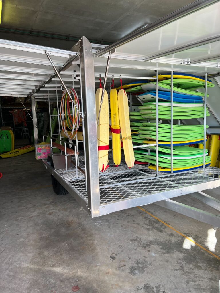 Surf club trailer loaded with equipment including rescue tubes, body boards. The lattice flooring allows excess sand to fall out of the trailer and open wheel arches allow for easy cleaning with a hose